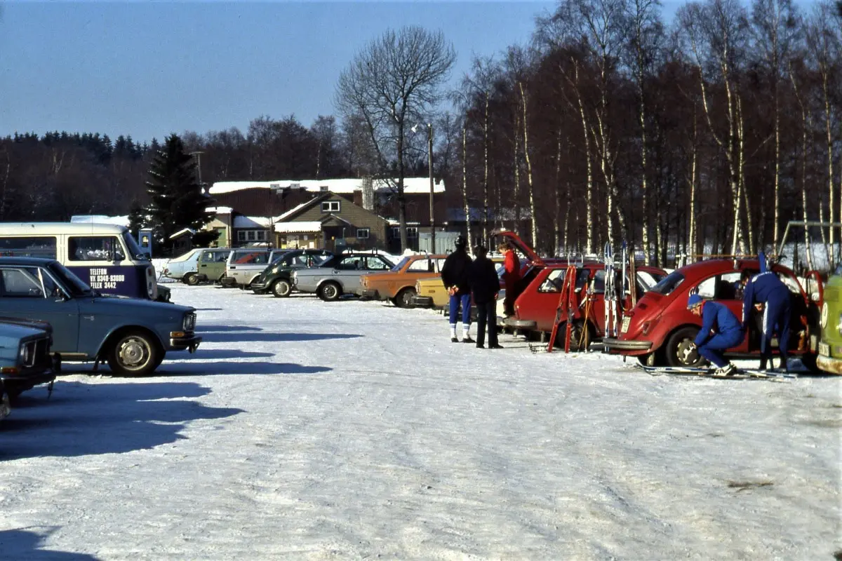 Vinter i Åkulla 1980. Parkeringen är full av bilar och skidåkare som tar på sig längdåkningsskidor.