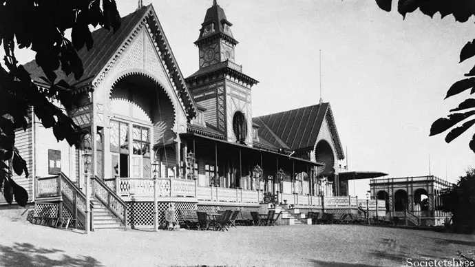 Societetshuset i Varberg. Svartvitt foto från år 1883-1885. Pampig byggnad med torn och spetsiga takdelar. Stor veranda längs husets framsida.