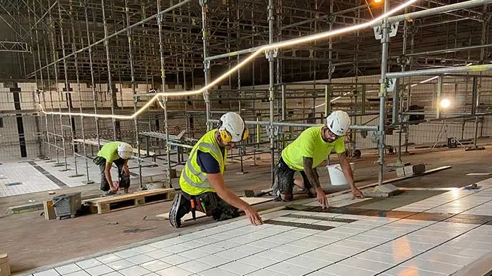 Tre arbetare sätter kakelplattor i 50-metersbassängens botten.
