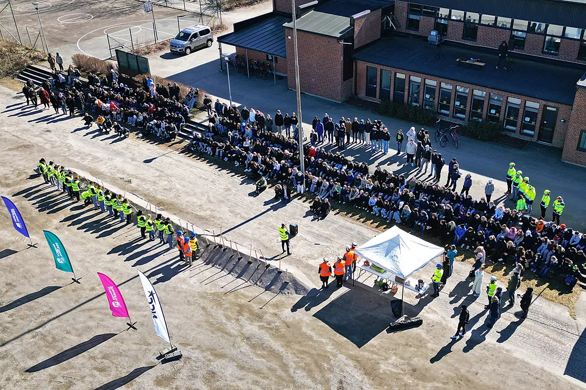 Bild tagen från luften där personer står uppradade framför en publik och en lång grushög. I bakgrunden syns den nuvarande Håstensskolan. 
