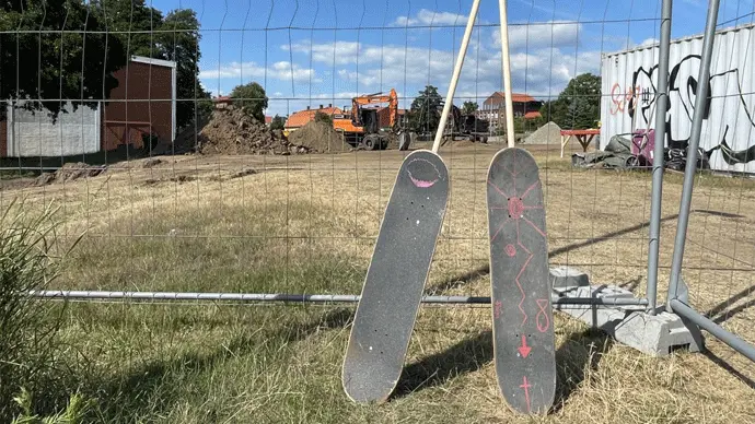 Två spadar gjorda av skateboards står lutade mot ett gallerstaket.