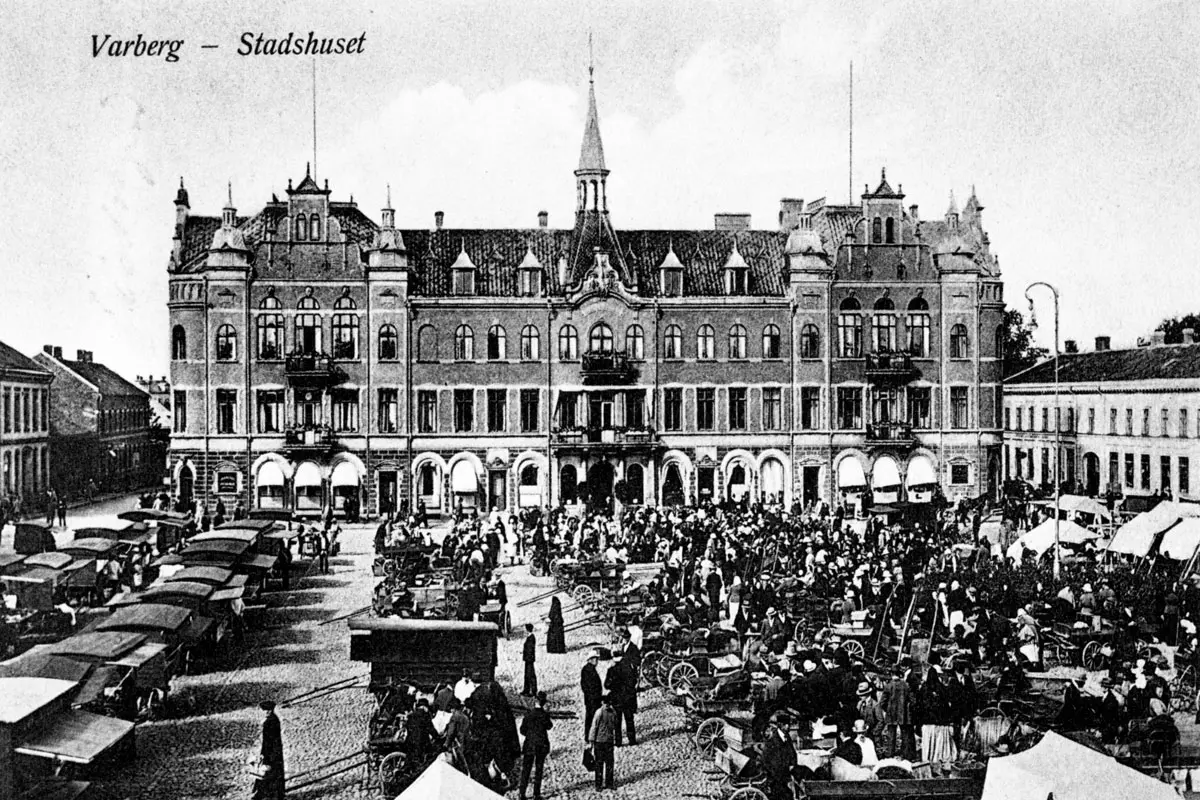 Historisk svartvitt foto på Varbergs stadshotell. I förgrunden ett gytter av människor, mnarknadsstånd och lastvagnar 