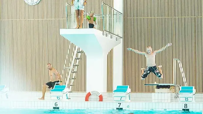 Hopptorn och trampolin i simhallen Pingvinen. Ett barn hoppar från trampolinen med armarna rakt ut i luften.