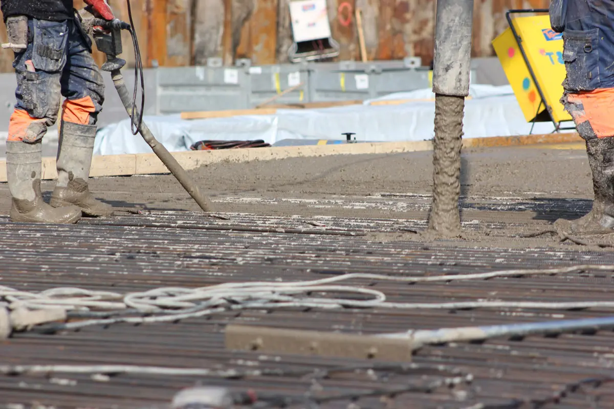 Närbild av gjutningsarbetet i kv Falkenbäck. Betong forsar ur en slang, två personer arbetar med att jämna till betongen.