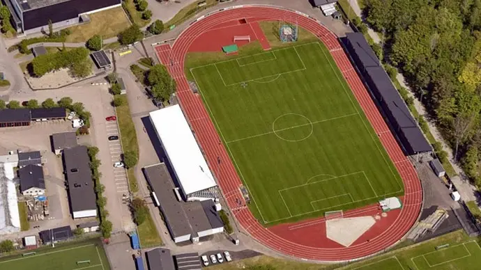 Drönarbild över Varberg Energi Arena. Bollplanen, en rektangulär gräsyta, omgärdas av orange löparbanor. Läktare på båda långsidorna.