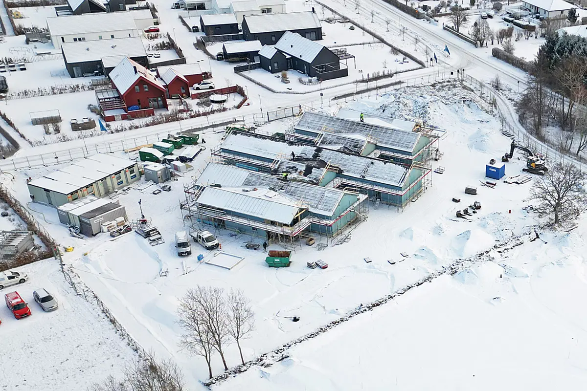 Drönarbild över byggarbetsplatsen. Snö på marken. Tre huskroppar är sammanbyggda. 