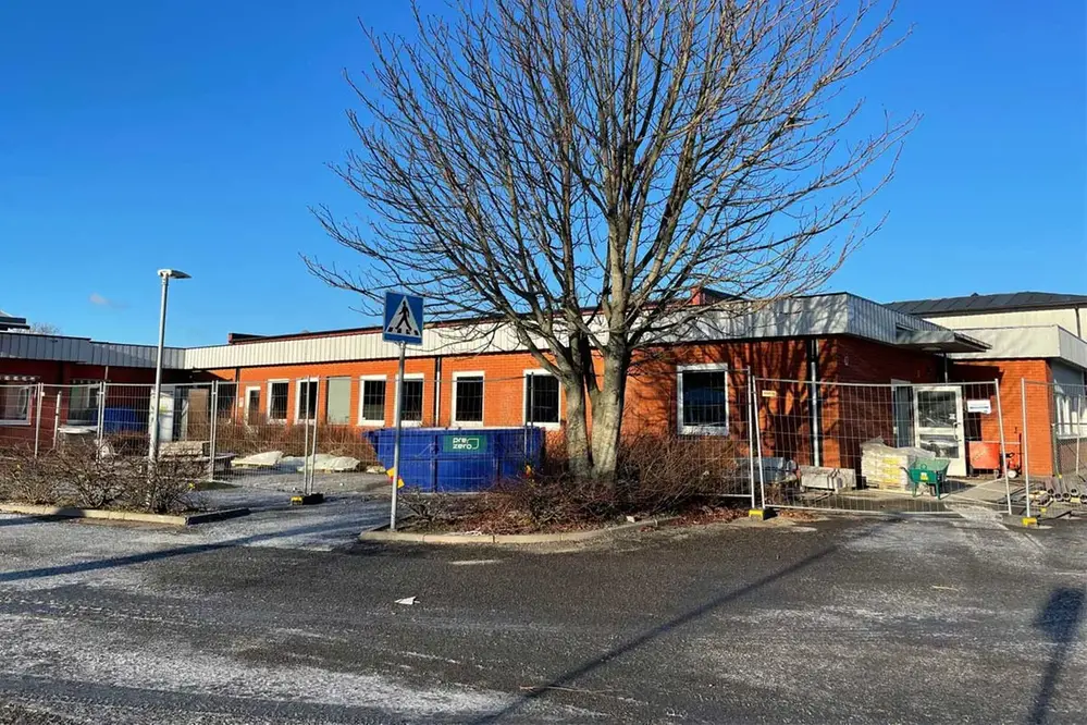 Buaskolan i Varberg. En orange tegelbyggnad med platt tak. En vinterbild med frost på vägen. Ett stort träd mitt i bilden, kalt utan löv.