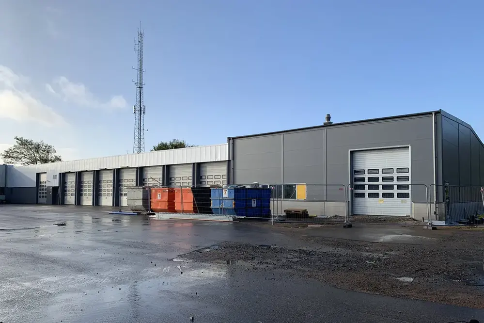 Nya tvätthallen och vagnhallen, Räddningsstationen i Varberg. Hög byggnad i grå plåt sammanbyggd med lägre i ljusare grå. Sju stora portar för brandbilars passage.