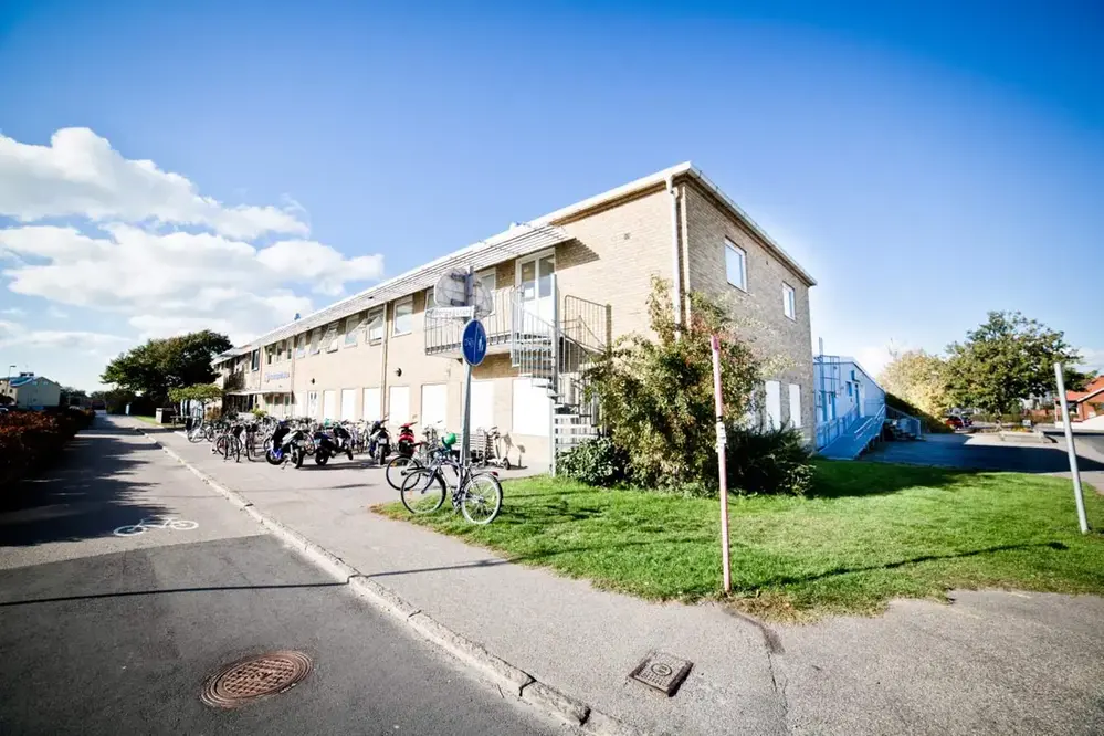 Kvarteret Björnen i Varberg. En gul tegelbyggnad i två våningar omgiven av gröna gräsmattor och träd. Cyklar står parkerade utanför huset.